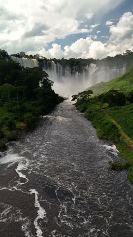 Breathtaking high aerial shot of the massive crescent-shaped Kalandula Falls plunging over a rocky cliff with rising mist surrounded by lush green wilderness in Angola, Africa.