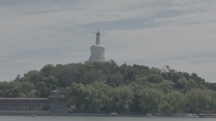 Pan left shot from the historic White Pagoda on Qionghua Islet across the lake, revealing a modern Beijing skyline featuring the CITIC Tower (China Zun) in the distance.