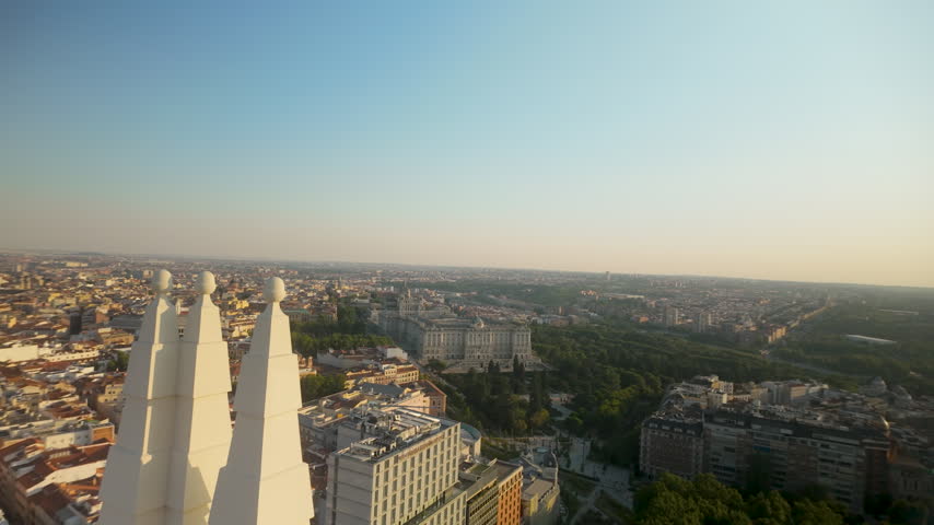 A cinematic aerial sweep over Madrid, Spain, featuring the Royal Palace, lush green parks, and urban architecture during a warm sunset. Ideal for travel documentaries and European city promos.