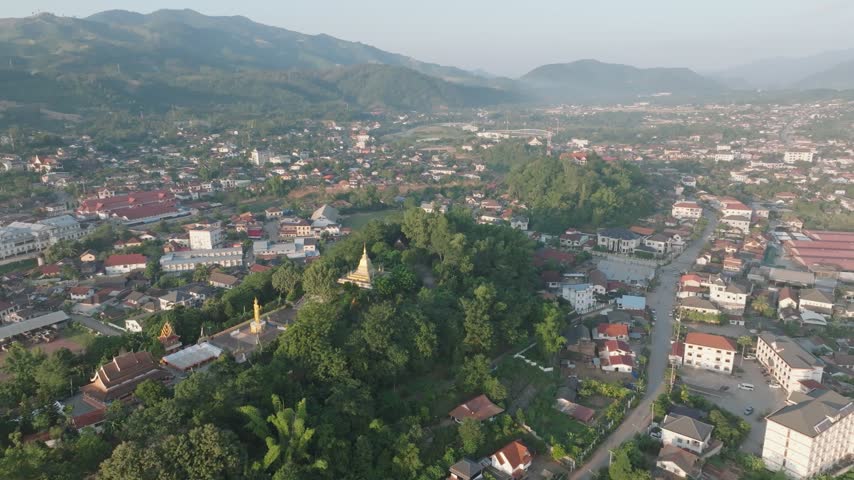 Aerial view of a provincial town with a hilltop temple and golden stupa surrounded by mountains, northern Laos
