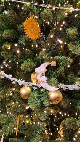 Close-up of decorated Christmas tree branch featuring golden sun ornaments, crescent moon and golden apples, whimsical festive design.
