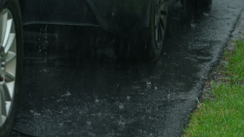 Heavy rain splashing on wet asphalt around parked cars during an intense summer storm.