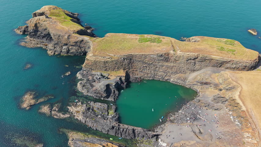 Aerial view of Blue Lagoon near Abereiddy in West Wales, people swimming and paddleboarding in emerald water surrounded by slate quarry cliffs