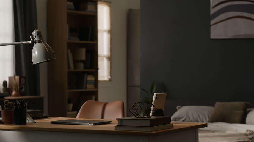 Empty home office desk setup with closed laptop, smartphone, and stationery appearing during camera pan. Clip suitable for remote work, hybrid job, and e-learning campaigns