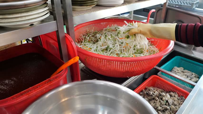 Culinary preparation involving raw seafood combined with shredded fresh vegetables and spicy red seasoning inside a large steel bowl for restaurant serving