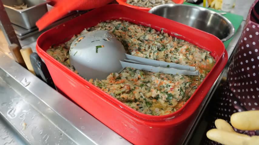 Freshly harvested raw oysters are combined with shredded vegetable mixtures and mixed thoroughly inside a large metal bowl within a professional commercial food preparation kitchen environment