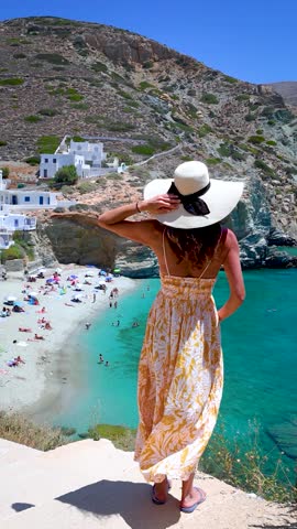 A tourist woman in a summer dress looks at the beach of Agali at Folegandros island, Cyclades, Greece, from a high viewpoint