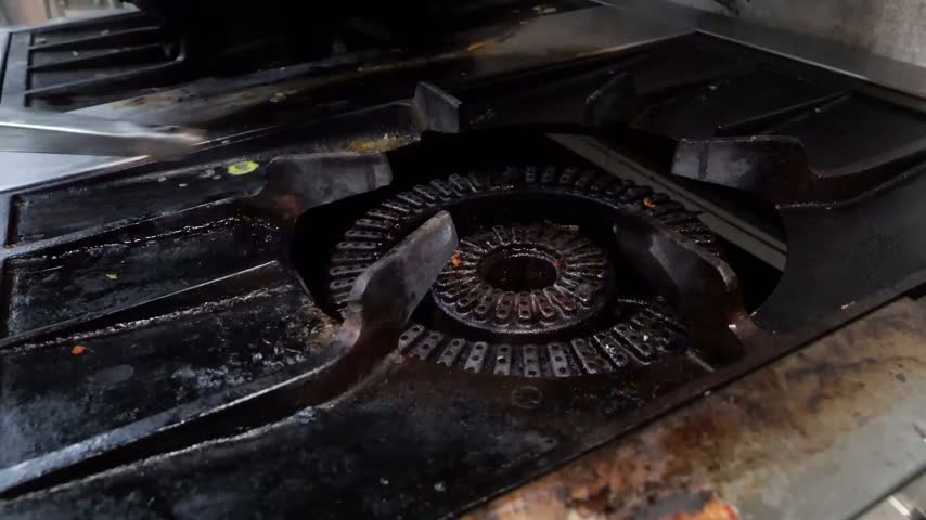 Lobster pieces are cooked in a frying pan with butter over open flames on a kitchen stove before being plated onto a white dish for fine dining service