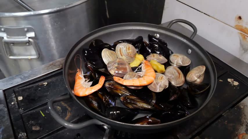 Delicious seafood soup preparation featuring assorted shellfish and fresh vegetables simmering over high heat in restaurant kitchen