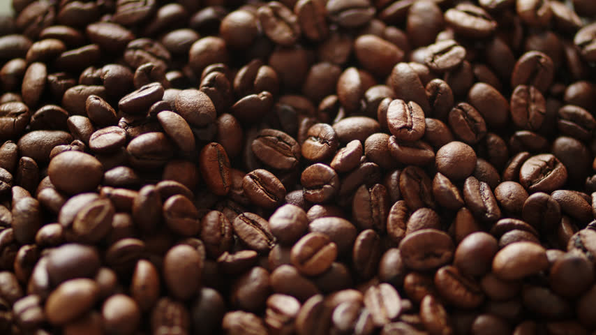 Spoon scooping roasted brown coffee beans from a pile. Close up texture of fresh aromatic arabica coffee beans with a silver spoon. Taking coffee beans from a pile with a spoon. 