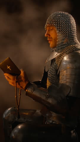 Vertical video of Caucasian young adult knight in armor holding Bible and rosary while praying. Perfect for historical documentaries, religious storytelling, and cinematic medieval trailers