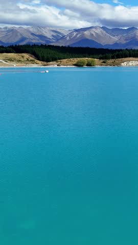Aerial view of turquoise Lake Pukaki with mountain range and blue sky in New Zealand.