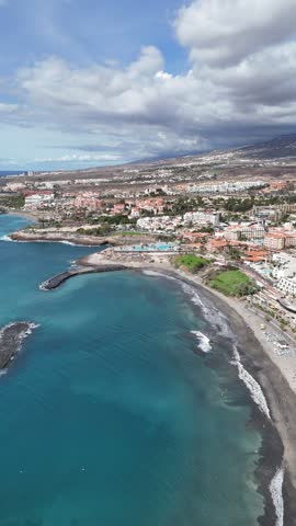 Drone view of Costa Adeje in Tenerife showing the turquoise Atlantic Ocean, sandy beaches, coastal resorts, residential areas and dramatic cloudy sky.
