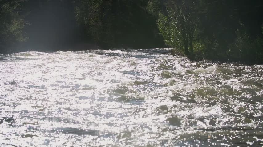 Back lit shot of kayaker riding down a raging river in the mountains