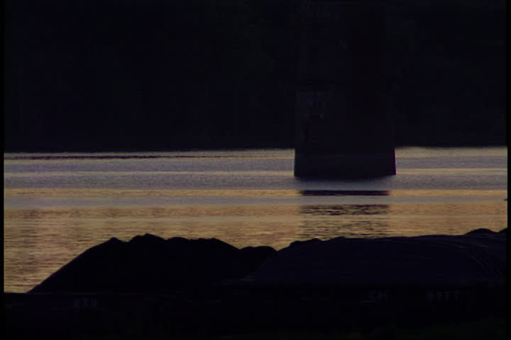 Pilot boat moves slowly along the Ohio River, past coal barges, at sunset in Metropolis, Illinois.