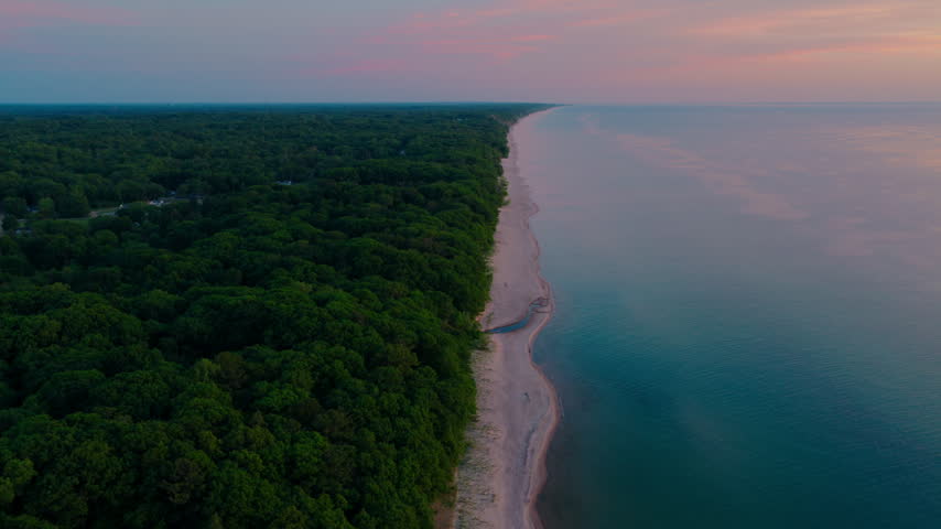 Michigan lakeshore at blue hour, with dense summer forest, a pale sand beach and glassy water stretching to a soft pink horizon.