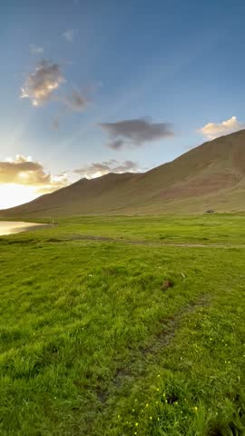 A peaceful early-morning landscape of Deosai National Park, showcasing the natural beauty of the high-altitude wilderness. Bright morning sunlight illuminates a beautiful lake in the foreground, while the surrounding open landscape creates a serene, scenic atmosphere. The footage captures the calm and untouched beauty of nature at sunrise.