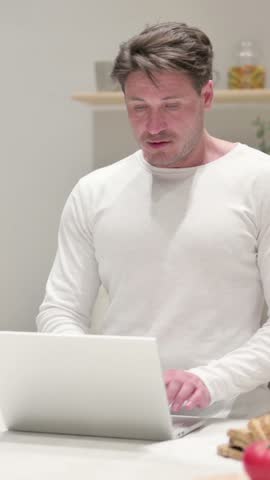 Middle Aged Man Celebrating Success while using Laptop in Kitchen