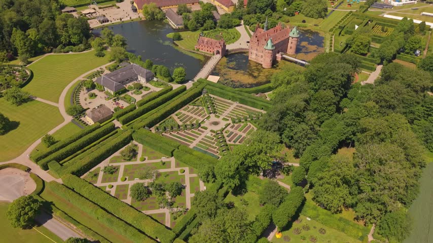 Aerial drone footage showcasing the historic Egeskov Castle surrounded by its beautifully designed gardens, landscaped grounds, and lush greenery in Denmark.