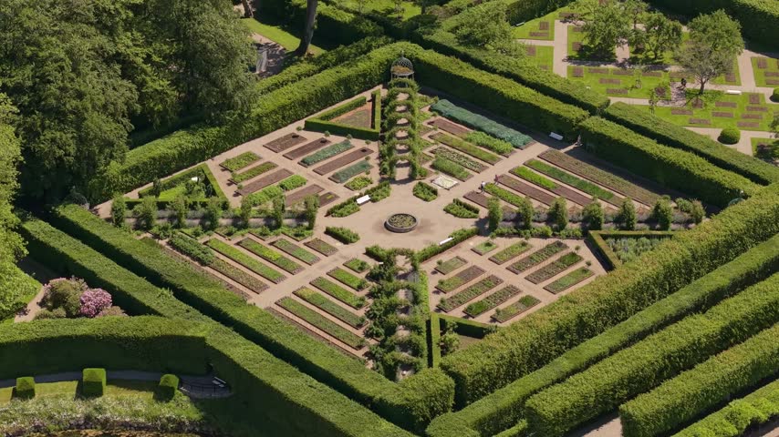 Drone orbit around the distinctive square garden of Egeskov Castle, showcasing its geometric design, manicured greenery, pathways, and historic surroundings.