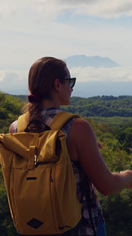 Young Female Traveler Looking Toward Distant Puncak Gunung Agung Across Tropical Landscape From Elevated Viewpoint On Nusa Penida.