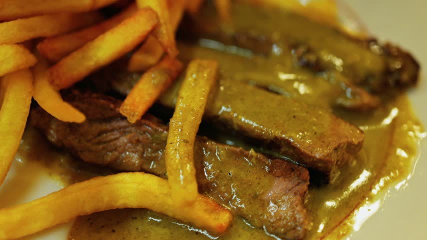 Delicious steak slices with crispy french fries, coated in smooth creamy sauce. Close-up view of gourmet meal presentation. Appetizing dish.