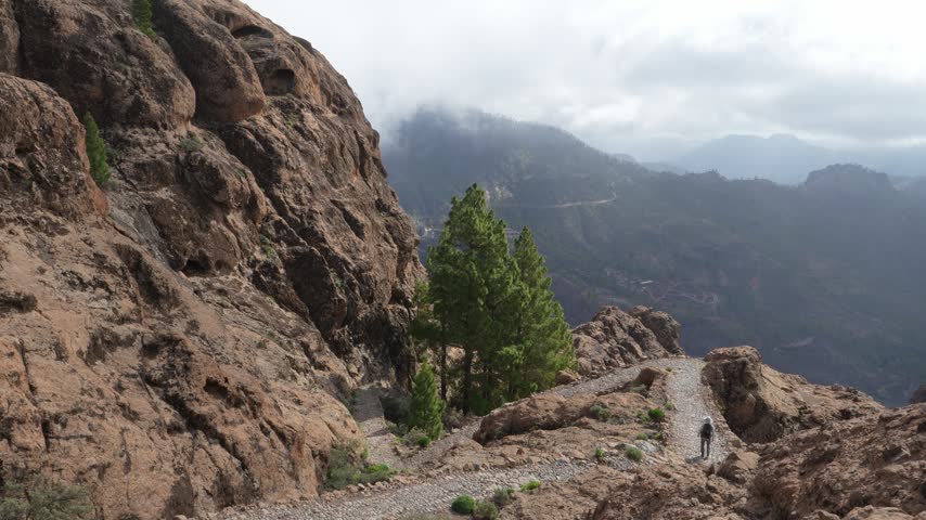 Hiker explores the dramatic volcanic terrain of Gran Canaria, Canary Islands. Enjoying an active adventure on a remote mountain path with panoramic views under a cloudy sky.