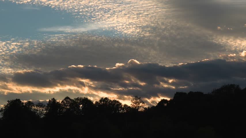 Clouds drifting across the sky above a dark tree lined landscape