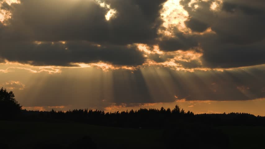 Dramatic clouds illuminated by sunlight above a dark rural landscape