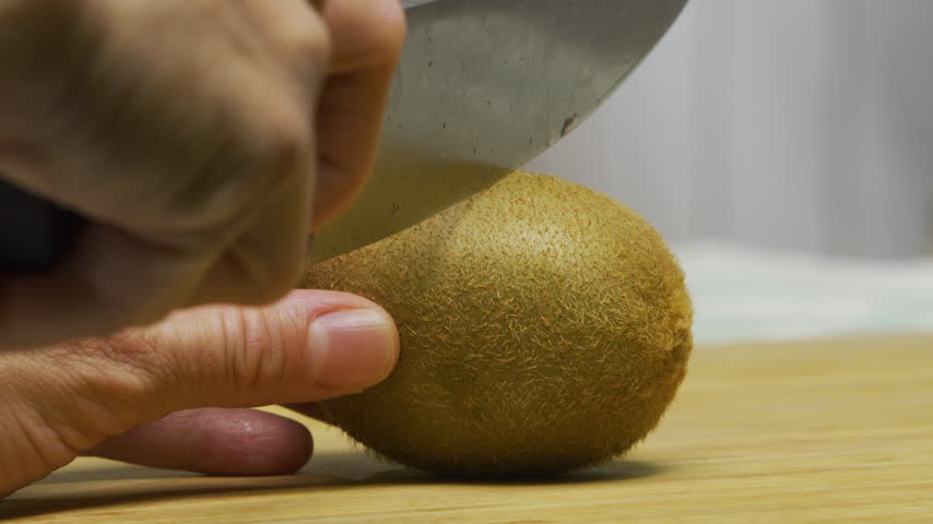 Cutting fresh kiwi in half with large knife - closeup shot