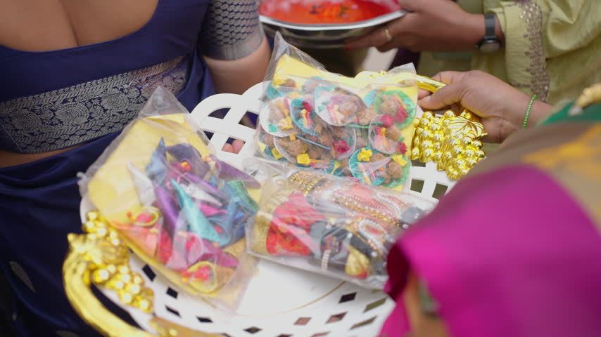 Guests hold a decorative tray filled with colorful packaged wedding favors during a South Indian Karnataka wedding ceremony.