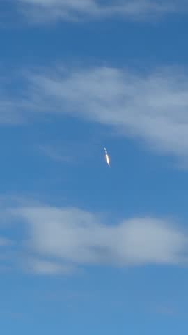 A rocket lifts off and climbs through a blue sky with soft white clouds. The bright flame, vertical ascent, and recorded sound create a dramatic aerospace launch video.