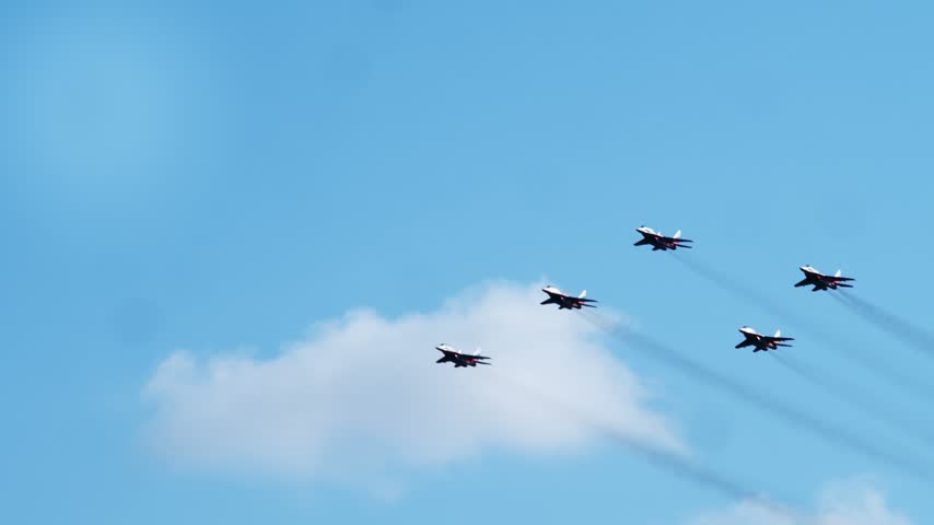 Five military fighter jets cruise across vivid blue sky in diagonal formation. Precision teamwork defines tactical flight display during national holiday celebration.