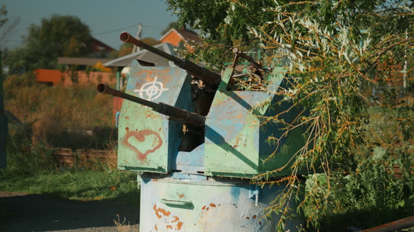 Obsolete, abandoned, and rusty combat guns with a heart painted on the body stand amidst the natural landscape. A graveyard of weaponry. An echo of war. The aftermath of war.