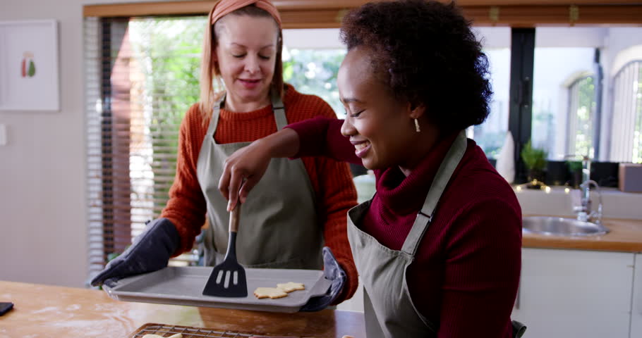 Diverse female friends preparing star cookies from cooling rack onto tray using spatula at counter. Baking, duo, kitchen, collaboration, teamwork, warmth, photorealistic