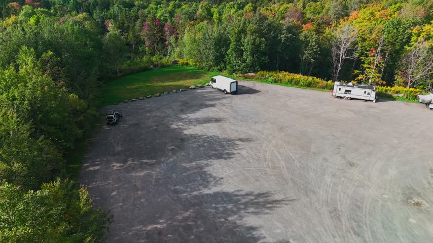 Aerial view of gravel parking area with campers and trailers near Hogback Mountain Conservation Area forest in early September autumn, representing rural travel and recreation.