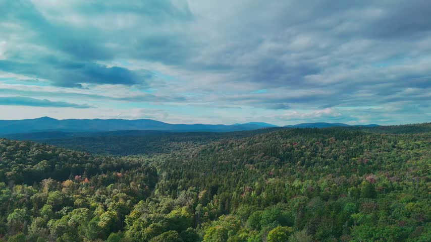 Aerial view of Hogback Mountain Conservation Area, Marlboro, Vermont with rolling forested hills, distant mountains, and dramatic cloudy sky, representing wilderness and environmental preservation. 4K.