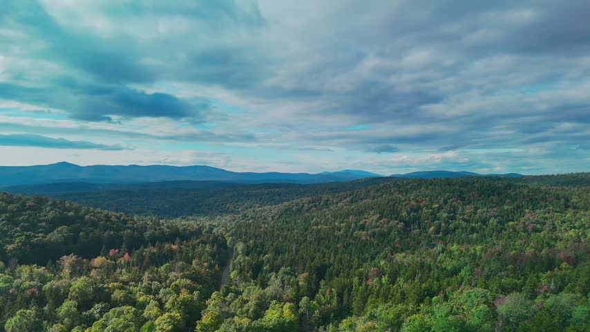 Scenic aerial view of Hogback Mountain Conservation Area, Marlboro, Vermont with rolling forested hills, distant mountains, and dramatic cloudy sky, representing wilderness and environmental preservation. 4K.