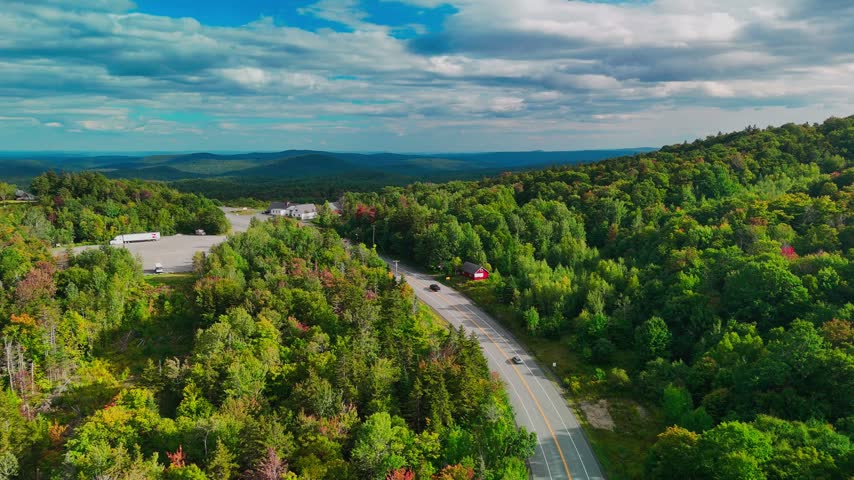 Aerial view of a winding road through Hogback Mountain forest, Marlboro, Vermont with rolling hills and distant mountains, representing wilderness, travel, and conservation. 4K.