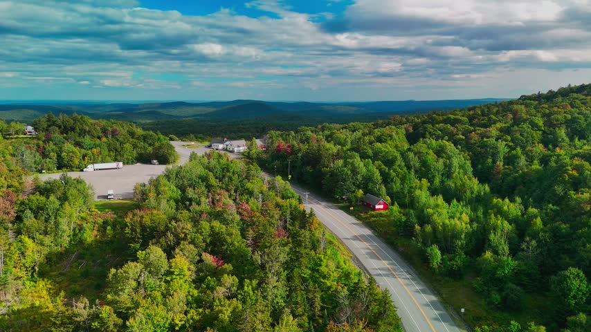 Aerial view of a winding road through Hogback Mountain forest, Marlboro, Vermont with rolling hills and distant mountains, representing wilderness, travel, transportation and conservation.