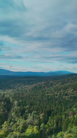 Scenic aerial view of Hogback Mountain Conservation Area, Marlboro, Vermont with rolling forested hills, distant mountains, and dramatic cloudy sky, representing wilderness and environmental preservation. 4K. Vertical.