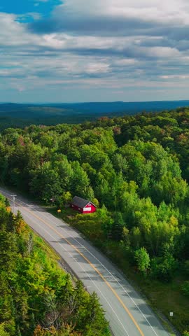 Aerial view of a winding road through Hogback Mountain forest, Marlboro, Vermont with rolling hills and distant mountains, representing wilderness, travel, transportation and conservation. Vertical.