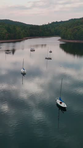 Aerial landscape of sailboats resting on calm Harriman Reservoir or Lake Whitingham in Vermont, USA, surrounded by lush forested hills under cloudy skies. Rlaxation, nature, and outdoor leisure. Vertical.