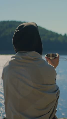 Close-up of a woman holding a cup beside Colebrook River Lake, CT, with forested hills and calm water, representing mindfulness, relaxation, and outdoor tranquility. Vertical.
