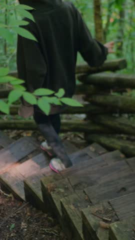 Hiker descending rustic wooden stairs on a forest trail, surrounded by green woodland. Outdoor hiking, nature travel, and peaceful adventure. 4K. Vertical.