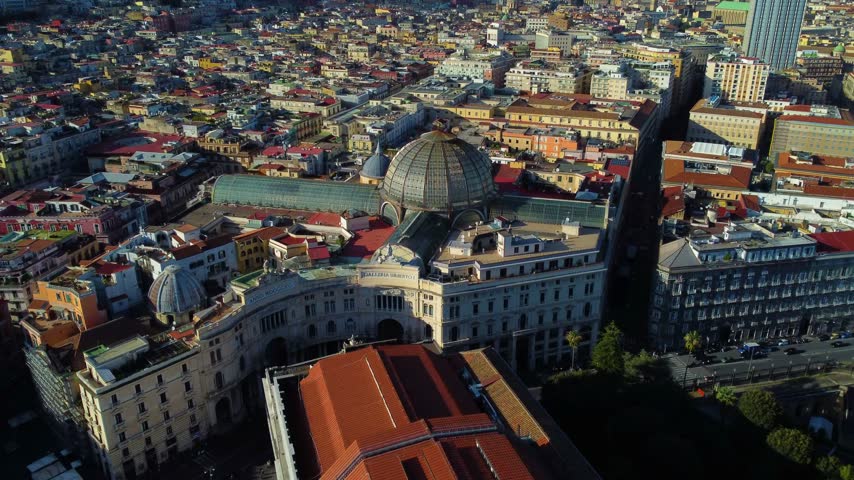 Aerial view of the historic Galleria Umberto I shopping gallery with its iconic glass dome surrounded by dense urban rooftops in Napoli, Campania, Italy.