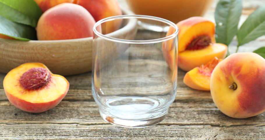 Pouring tasty peach juice into glass at wooden table, closeup