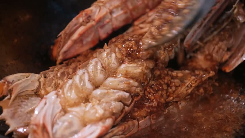 A high-quality, close-up stock shot of fresh mantis shrimp (mantis prawn) being tossed and stir-fried with minced garlic, ginger, and aromatic spices in a hot wok.