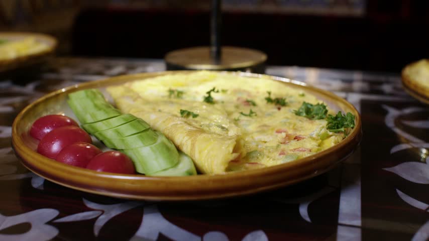 Hand using fork to serve omelette with cucumber and tomato on decorated table