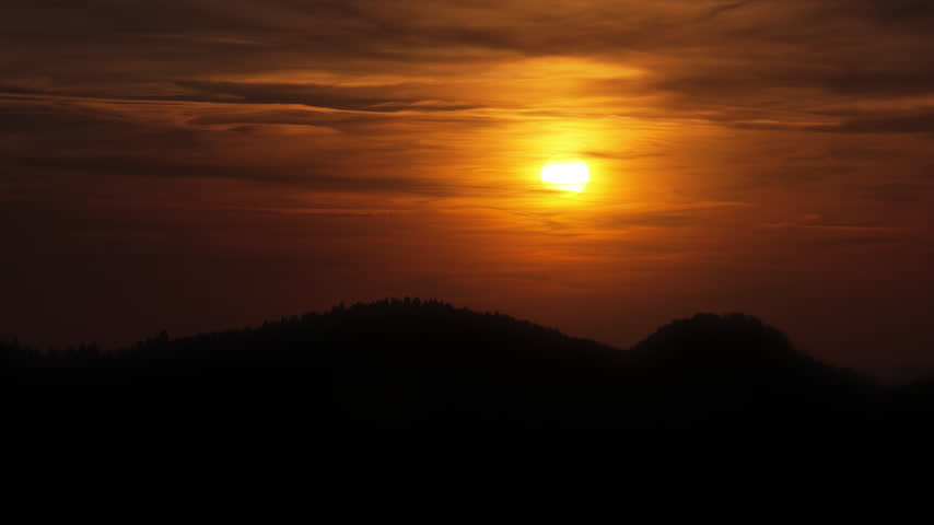 Aerial drone view of the sky glowing orange over darkened hills, in Romania, at dusk